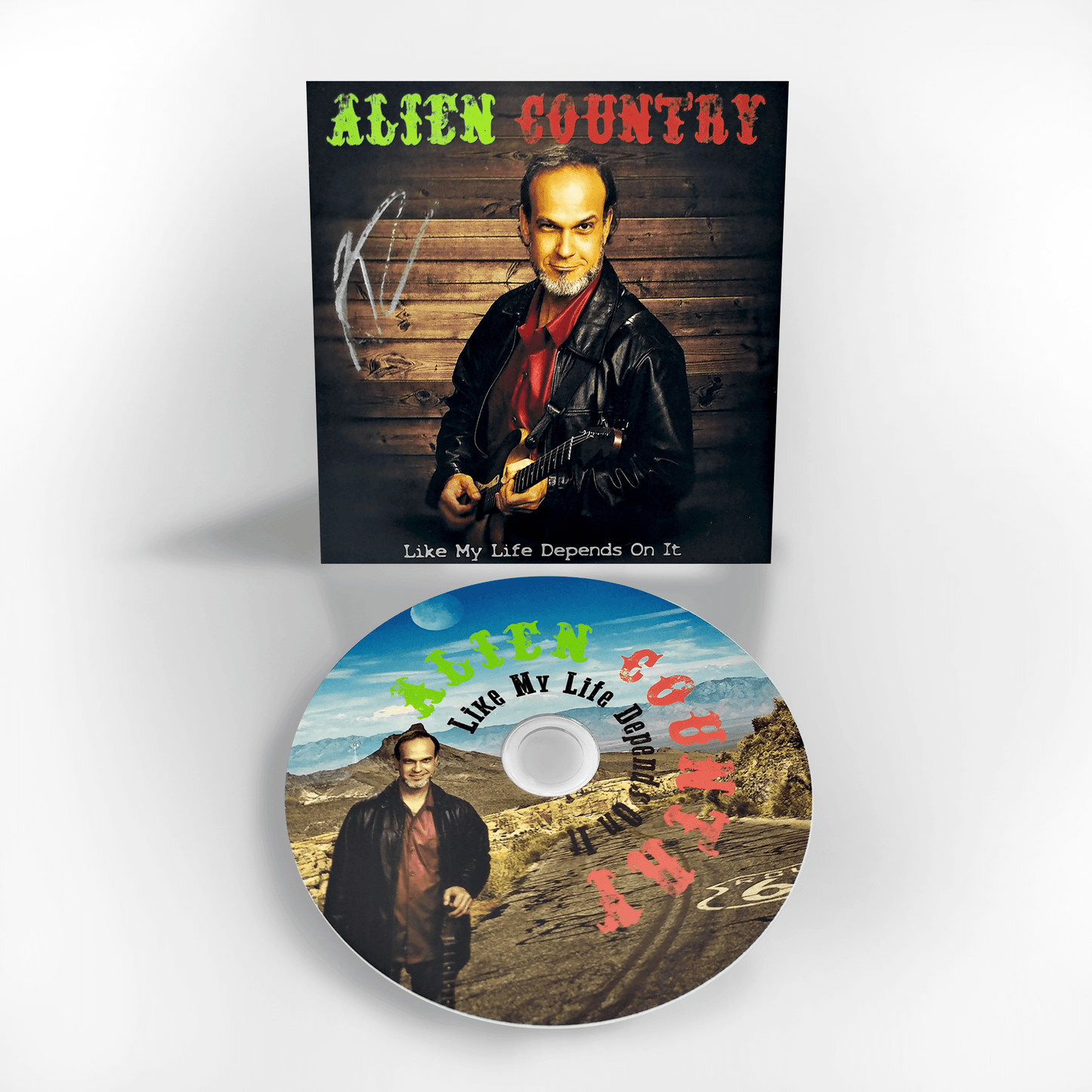A photo of a CD and it's sleeve. The Sleeve has a picture of Liam Marcus holding an electric guitar. The CD art is a picture of Liam Marcus standing on a scenic  highway with mountains in the background. Scifi country rock